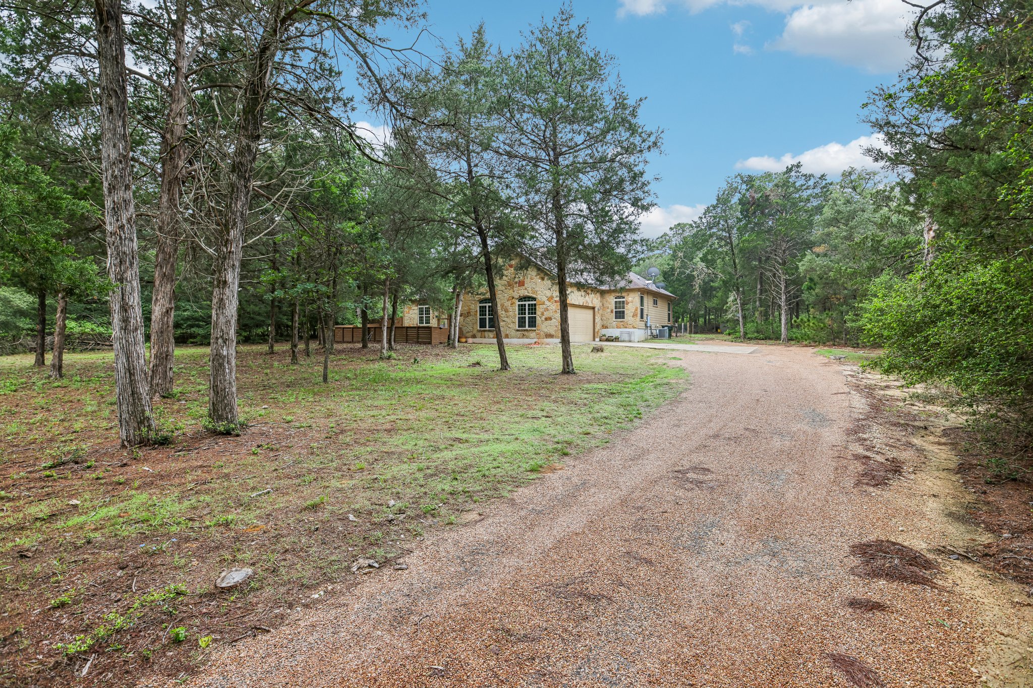 267 Corral Road Smithville, TX 78957 - Photo 9 of 40 Stone exterior residence featuring an attached garage and a gravel driveway