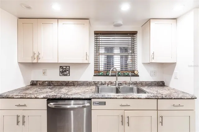 a kitchen with granite countertop stainless steel appliances white cabinets and a window