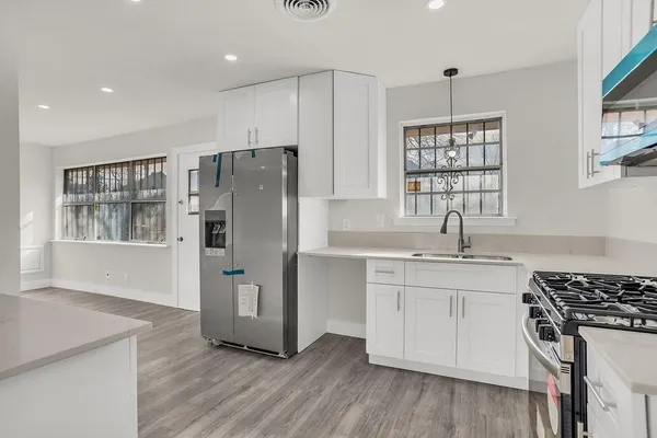 a kitchen with stainless steel appliances granite countertop a refrigerator a sink dishwasher a stove and white countertops with wooden floor