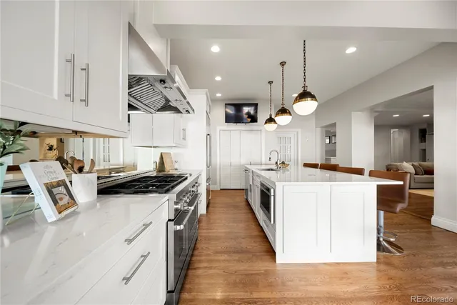 a large kitchen with stainless steel appliances kitchen island granite countertop a stove a sink dishwasher and white cabinets with wooden floor