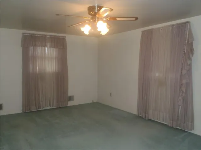 a view of an empty room with window and chandelier fan