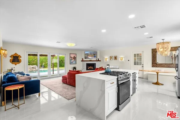 a kitchen with stainless steel appliances granite countertop a stove oven and a refrigerator with couches next to a large window