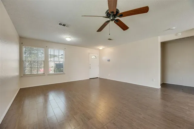 an empty room with wooden floor fan and windows