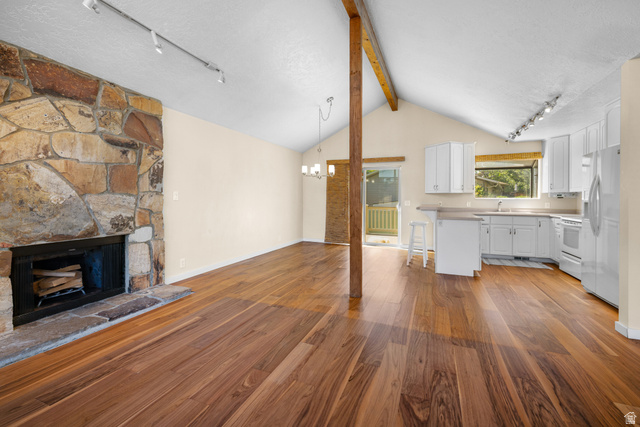 2088 Falcon Way Sandy, UT 84093 - Photo 6 of 46 Vaulted ceiling interior featuring wood-finish flooring, a stone-faced fireplace, exposed beam, white cabinetry, and a sliding glass door leading to an exterior balcony