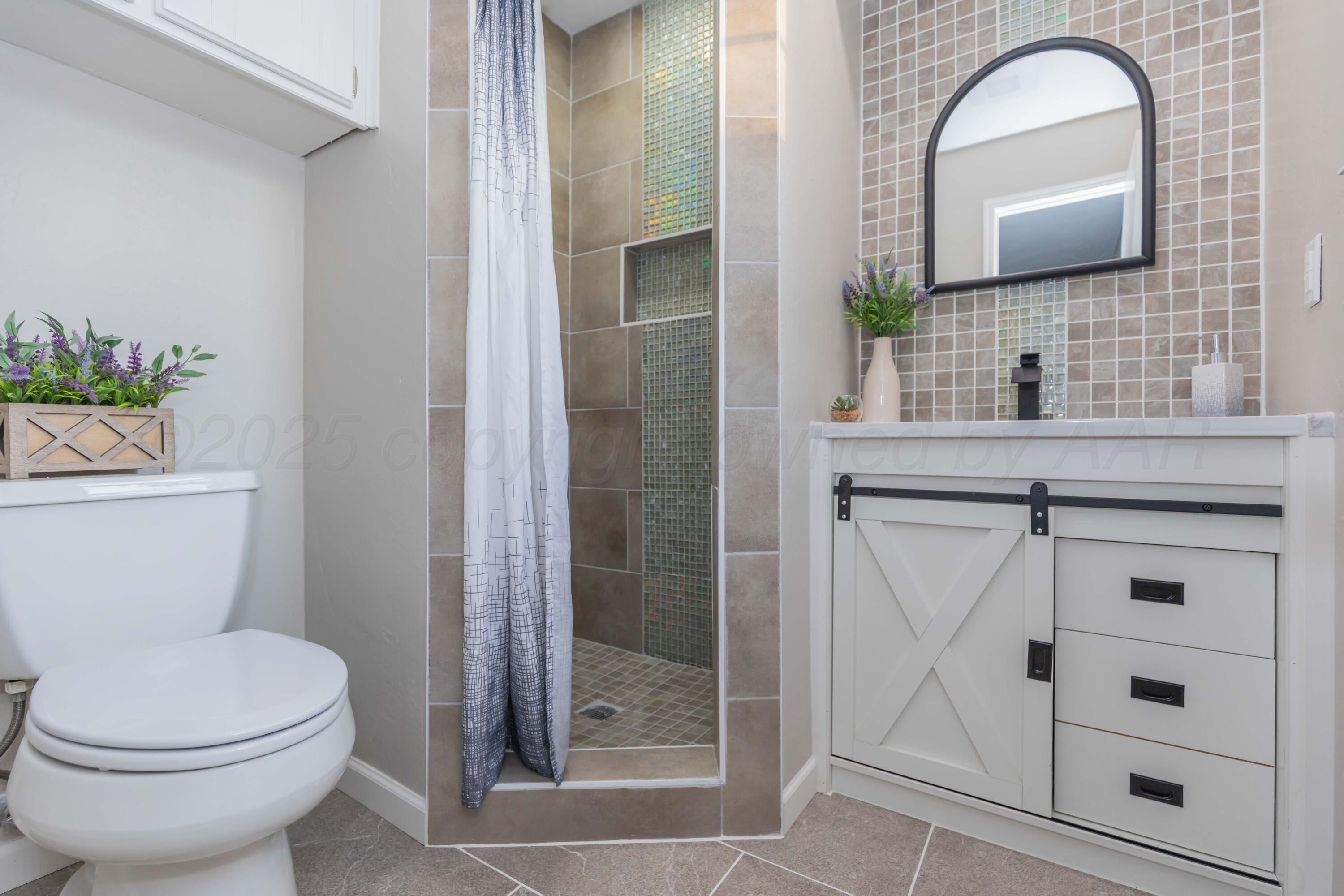 7912 Gerald Drive Amarillo, TX 79121 - Photo 23 of 45 a bathroom with a toilet a sink a mirror and shower