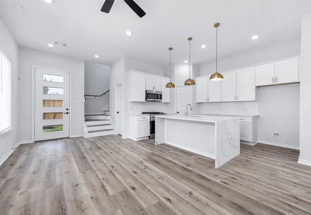 a large kitchen with white cabinets stainless steel appliances a sink and wooden floor