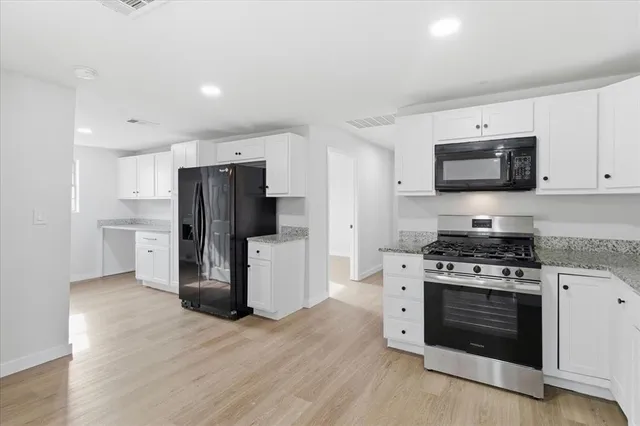 a kitchen with stainless steel appliances a stove a refrigerator a microwave a sink and white cabinets with wooden floor