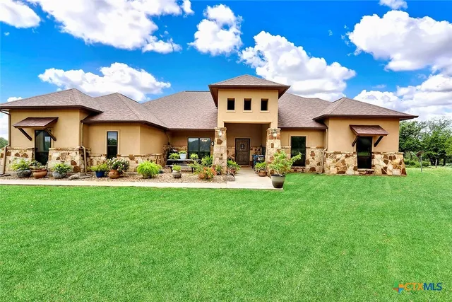 a view of a white house with a big yard plants and large trees