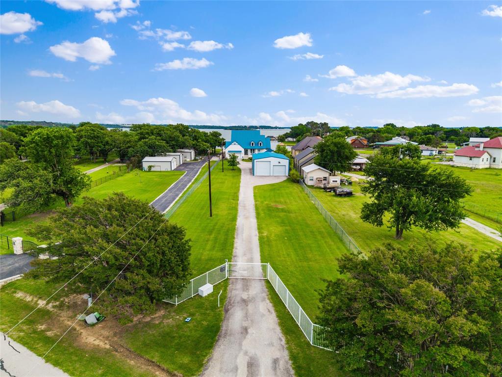 6625 Sandy Beach Road Azle, TX 76020 - Photo 37 of 40 Aerial view features gated driveway access leading toward the main residence, detached garage, and guest house structures. Expansive lawn areas, perimeter fencing, mature trees, and surrounding waterfront areas are visible throughout the property.