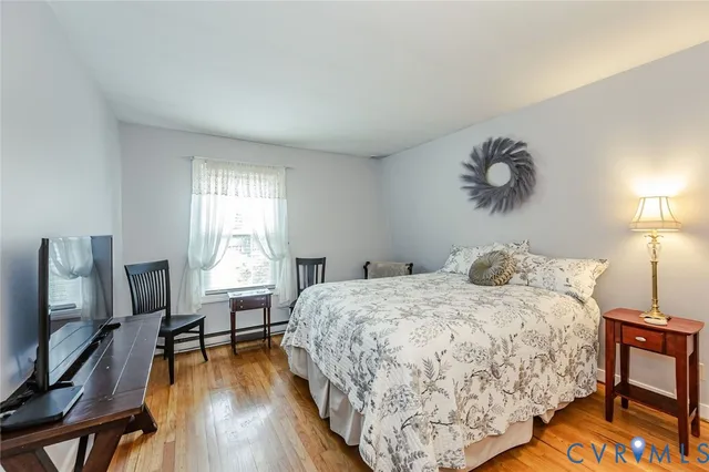a bedroom with a bed a flat screen tv and a exposed radiator with wooden floor