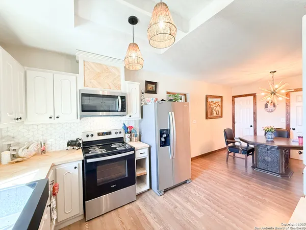 a kitchen with stainless steel appliances a stove top oven a sink dishwasher a dining table and chairs with wooden floor