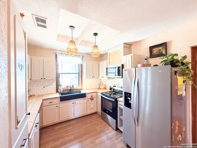a kitchen with stainless steel appliances a refrigerator a sink dishwasher a oven with white cabinets and wooden floor