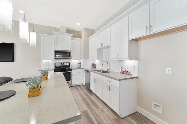 a kitchen with stainless steel appliances a stove top oven a sink a refrigerator white cabinets and wooden floor