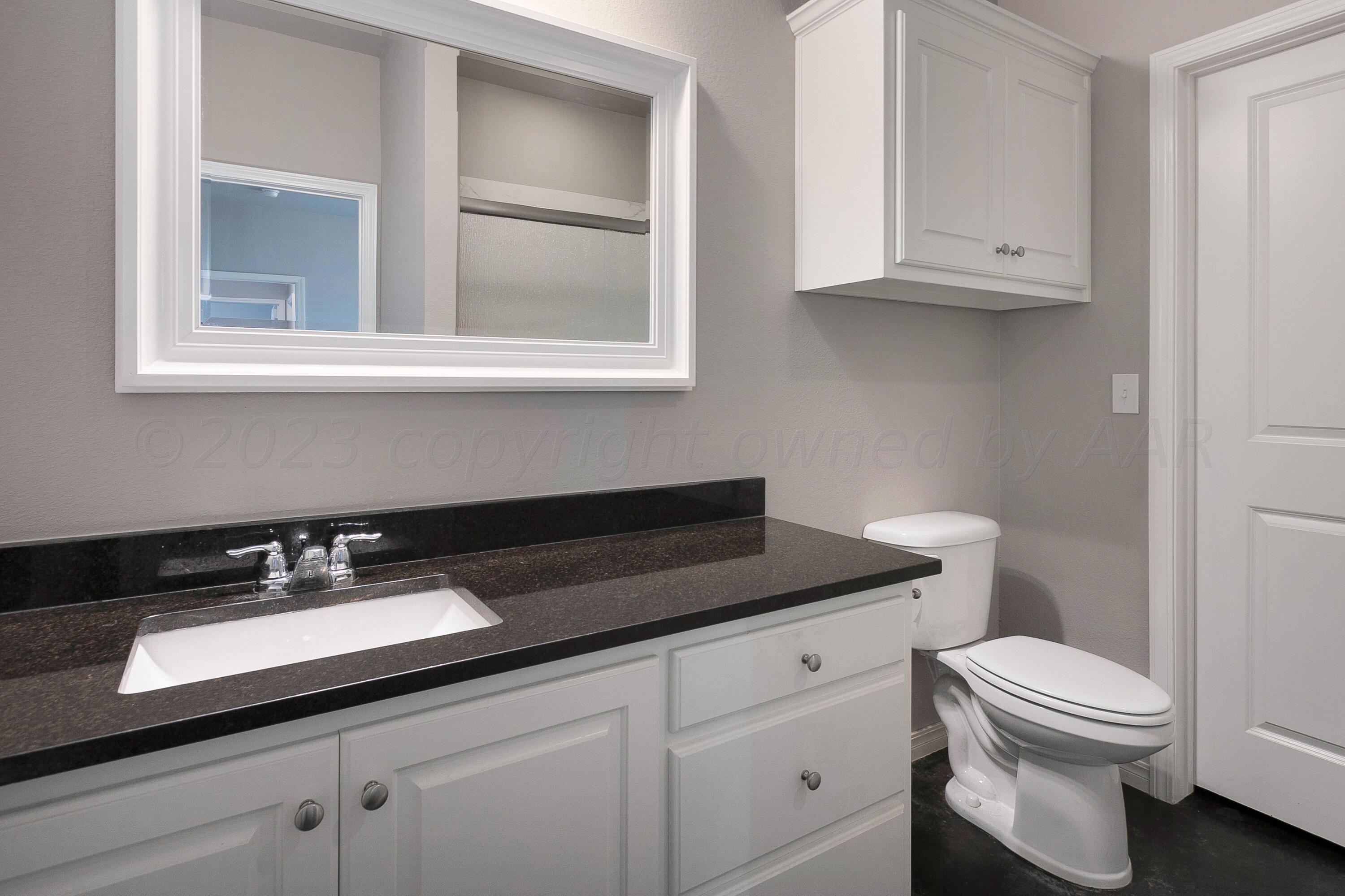 9927 Perry Avenue Amarillo, TX 79119 - Photo 14 of 24 a bathroom with a granite countertop toilet a sink and a mirror