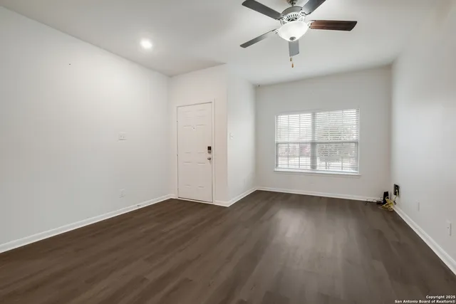an empty room with wooden floor chandelier fan and windows