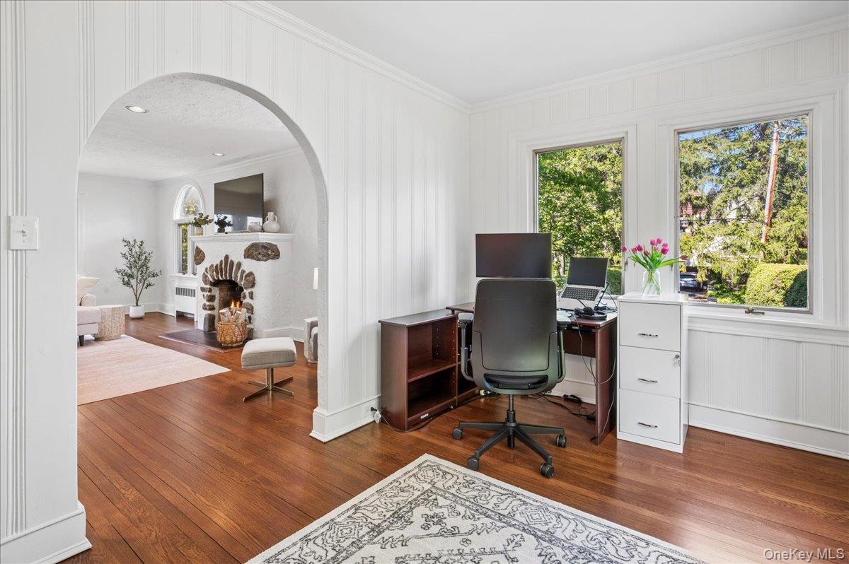62 Broadfield Road New Rochelle, NY 10804 - Photo 20 of 41 Hardwood flooring in a versatile study, featuring an arched doorway opening to a living area with a stone fireplace