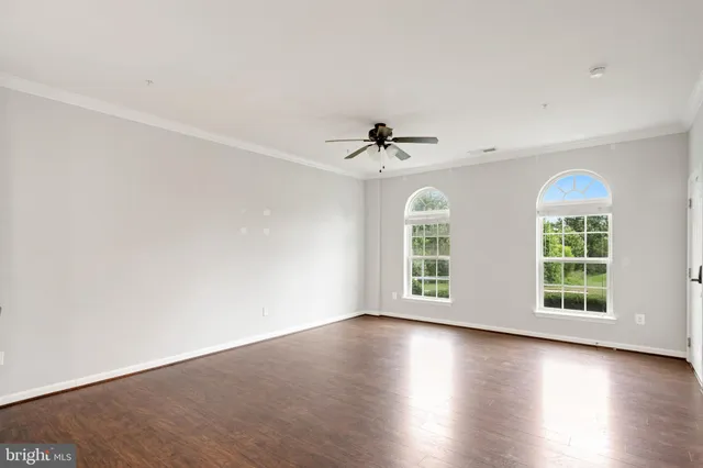 an empty room with wooden floor chandelier fan and windows