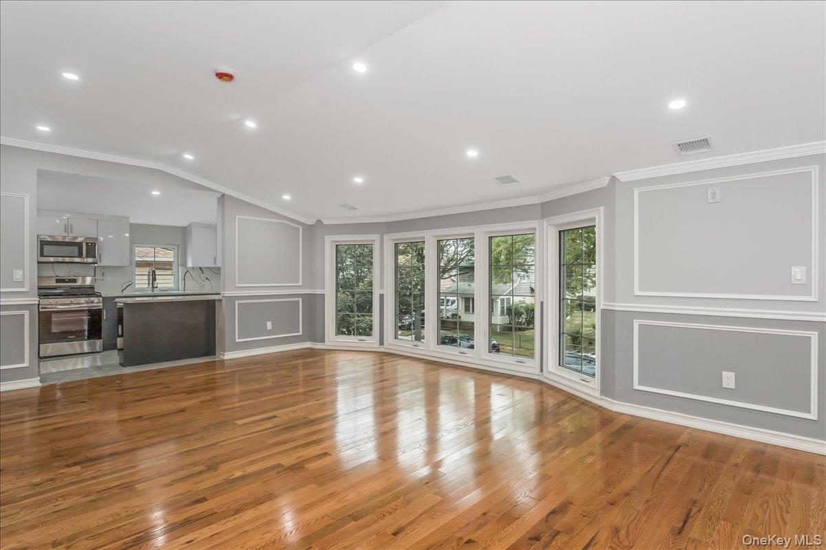 243-36 Caney Road Queens, NY 11422 - Photo 16 of 30 Unfurnished living room featuring plenty of natural light, light wood finished floors, a decorative wall, ornamental molding, and vaulted ceiling