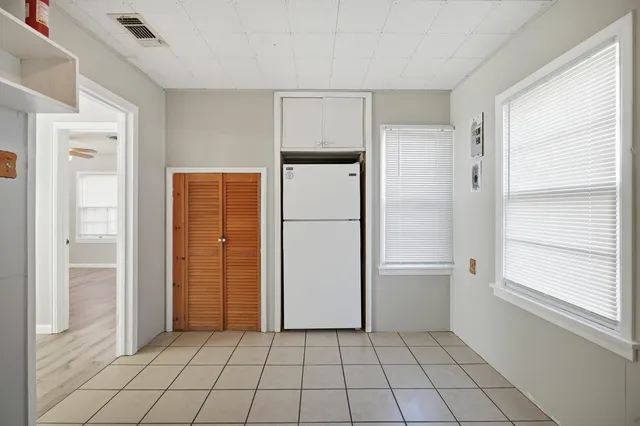 a view of a refrigerator in kitchen and an empty room in wooden floor