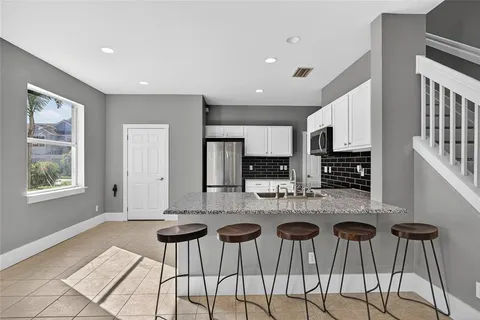 a kitchen with stainless steel appliances kitchen island granite countertop a dining table chairs and a refrigerator