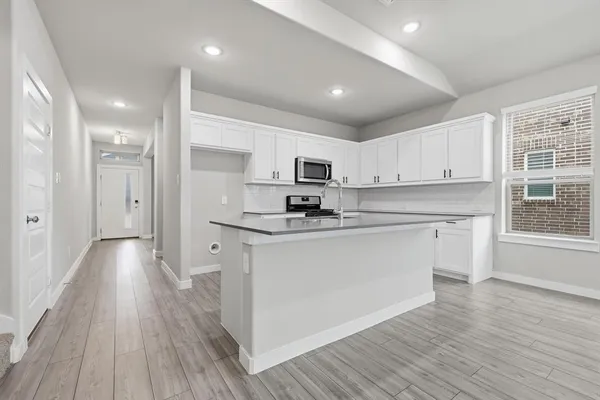 a kitchen with stainless steel appliances granite countertop a refrigerator a stove top oven a sink and white cabinets with wooden floor