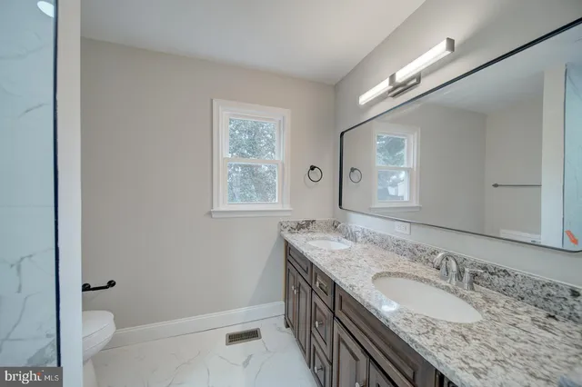 a bathroom with a granite countertop double vanity sink a mirror and a shower