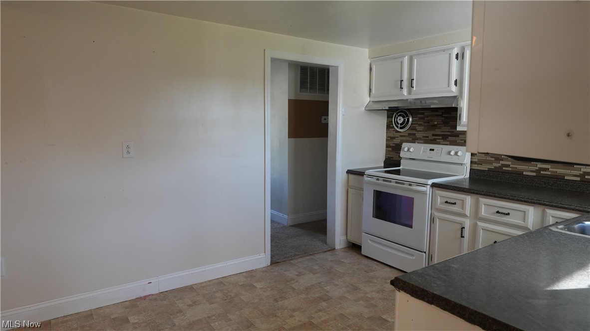 Kitchen with tasteful backsplash, light tile floors, white electric stove, and white cabinets