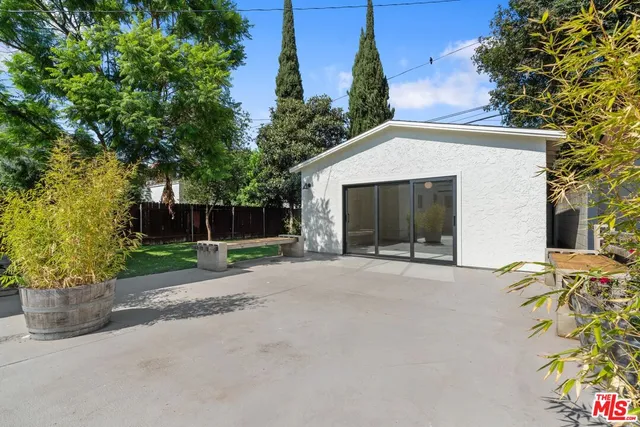 a backyard of a house with lawn chairs plants and large tree