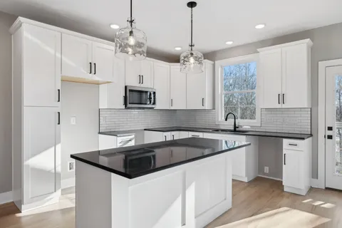 a kitchen that has a sink a microwave oven a stove and white cabinets with wooden floor
