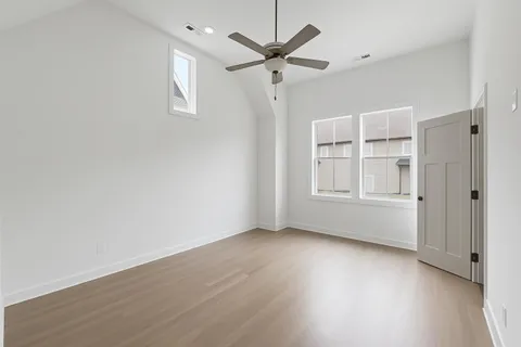 an empty room with wooden floor ceiling fan and windows