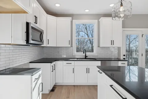 a kitchen with granite countertop a sink white cabinets and stainless steel appliances