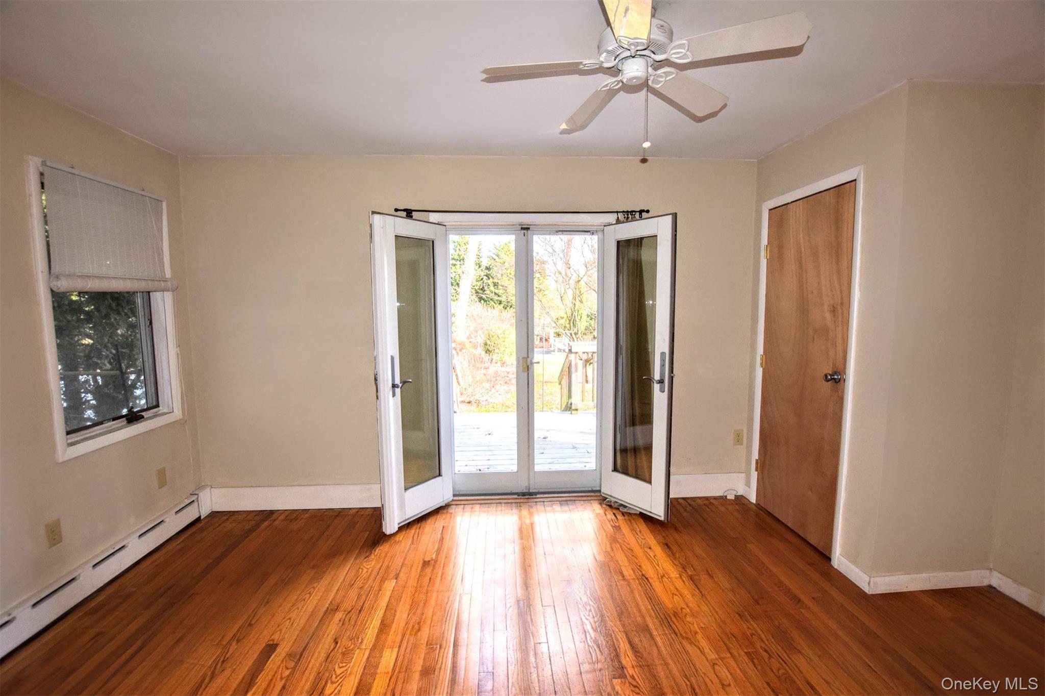 41 Country Club Road Bellport, NY 11713 - Photo 13 of 18 Empty room with a baseboard radiator, hardwood / wood-style floors, french doors, and a ceiling fan