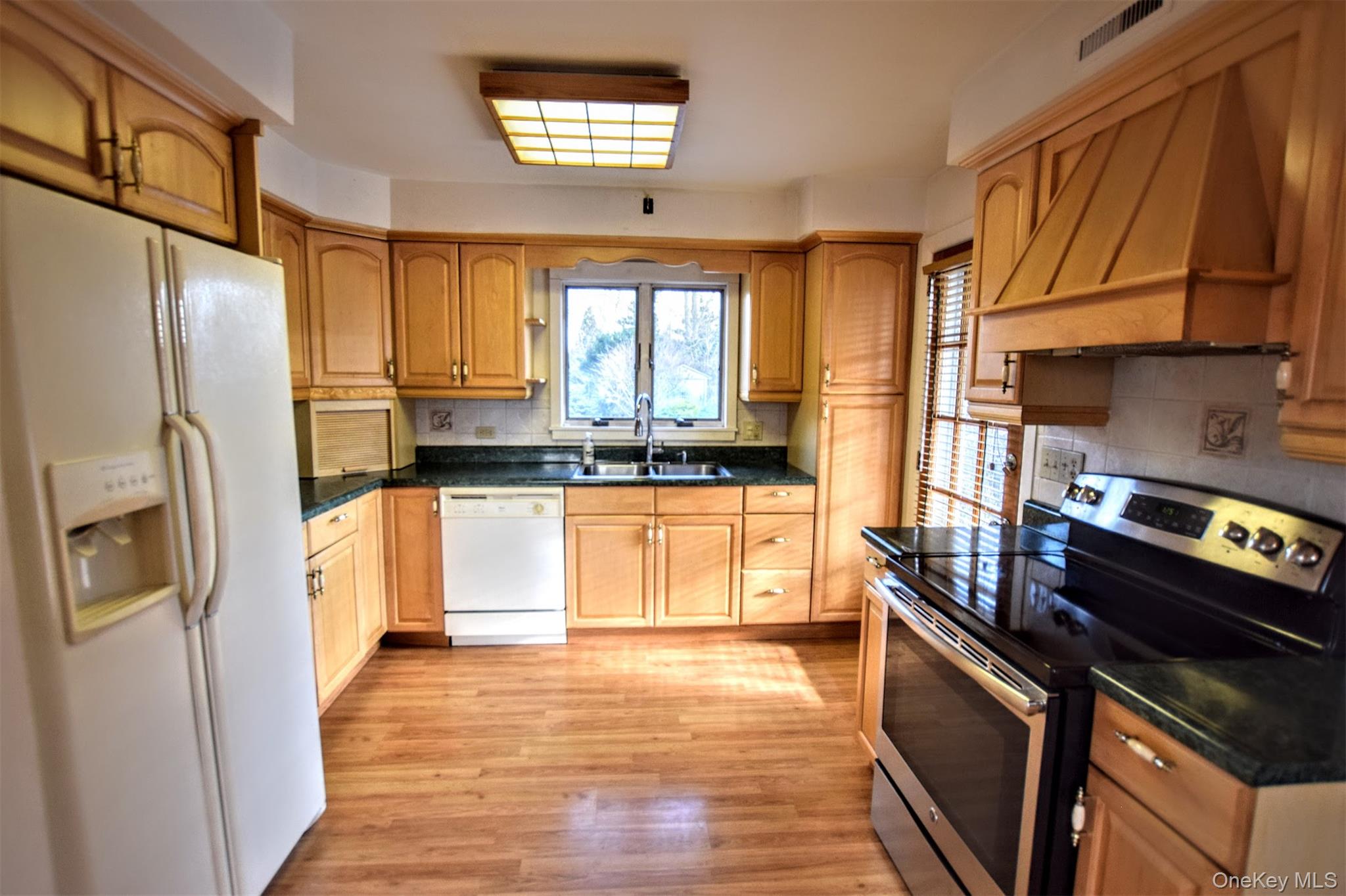 41 Country Club Road Bellport, NY 11713 - Photo 7 of 18 Kitchen featuring white appliances, custom range hood, light wood-type flooring, brown cabinetry, and decorative backsplash