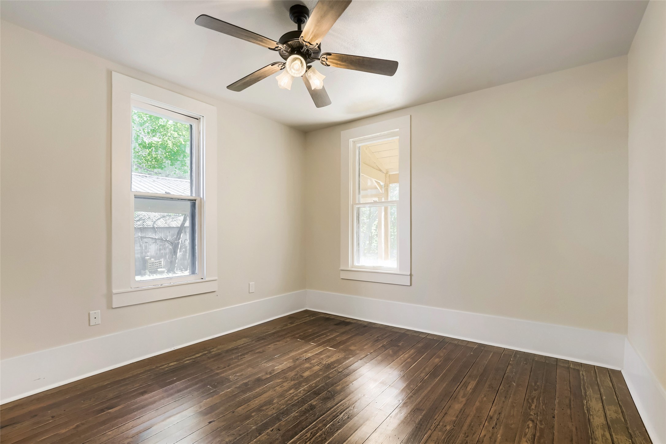 208 North Ave B Elgin, TX 78621 - Photo 16 of 29 Bedroom 1 features warm hardwood floors, two large windows for natural light, and a ceiling fan, creating a bright and airy atmosphere perfect for relaxation or use as a bedroom or office space.
