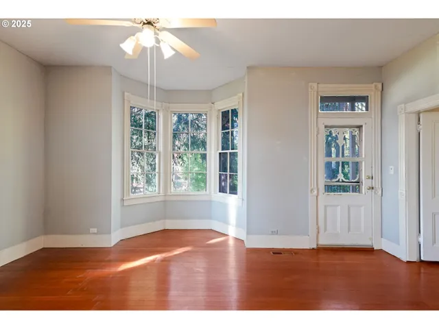 an empty room with wooden floor chandelier fan and windows
