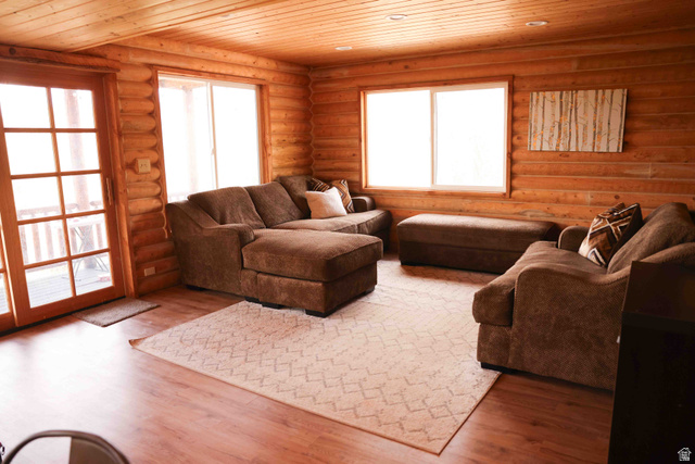 15253 Mill Road, Unit 62 Huntsville, UT 84317 - Photo 11 of 48 Living area featuring log walls, wood-finish flooring, a wood-paneled ceiling, and a glass sliding door opening to an outdoor area