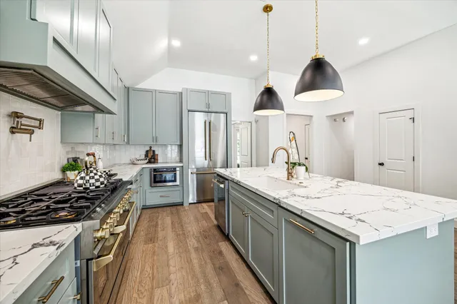 a kitchen with kitchen island granite countertop a sink a stove a refrigerator and island with wooden floor