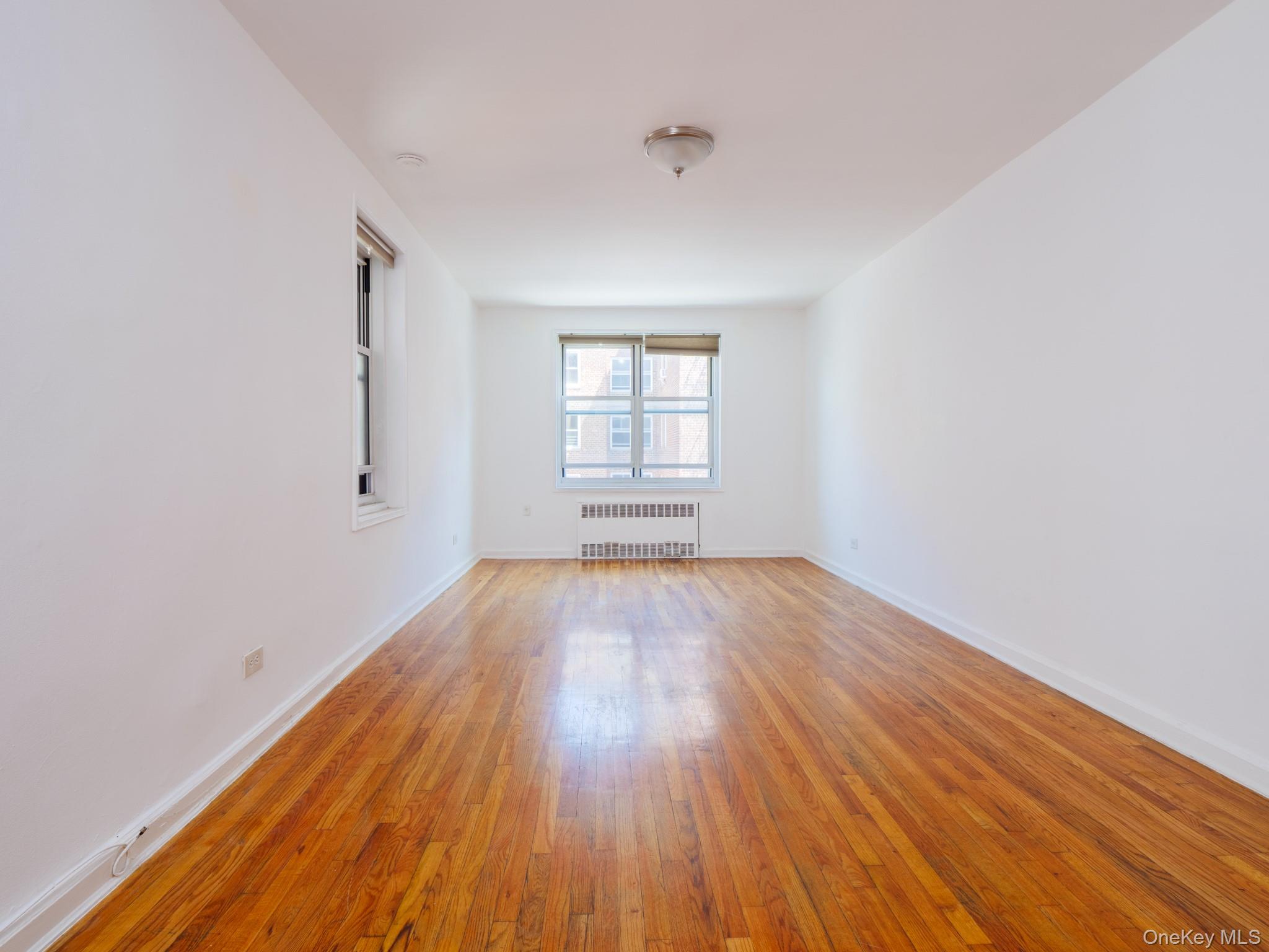 34-15 74th Street, Unit 4H Queens, NY 11372 - Photo 7 of 19 an empty room with wooden floor and windows
