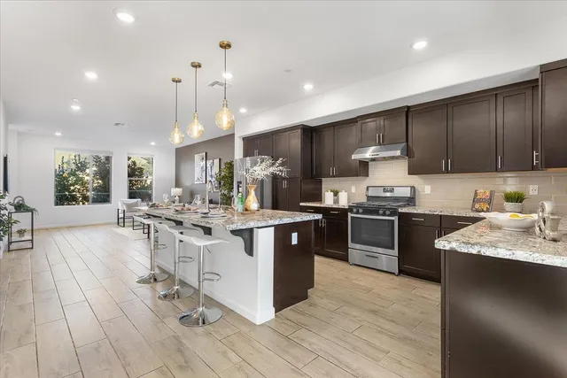 a kitchen with stainless steel appliances kitchen island granite countertop a large stove a sink dishwasher and a refrigerator with wooden floor