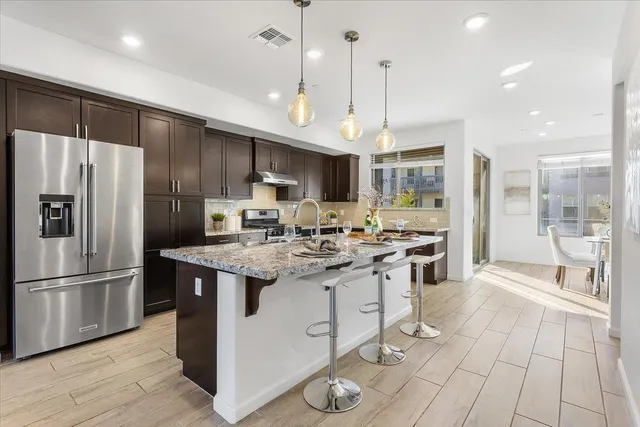 a kitchen with stainless steel appliances granite countertop a sink a stove a refrigerator and island with wooden floor