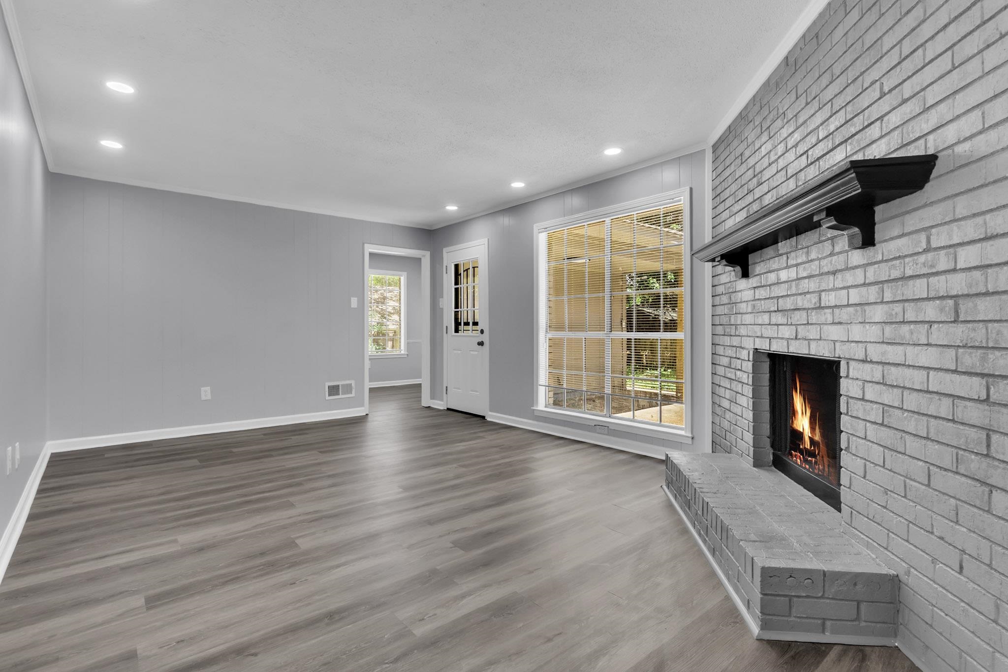 3314 Bright Ridge Cove Memphis, TN 38115 - Photo 6 of 16 Spacious living area featuring a gray brick fireplace with a dark wood mantel, large multi-pane windows, and wood-finish flooring