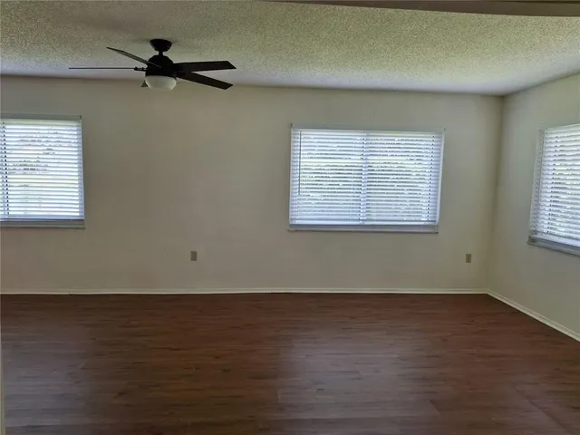 an empty room with wooden floor ceiling fan and windows