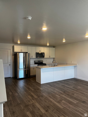 562 Hal Street, Unit 152 Tooele, UT 84074 - Photo 4 of 44 Contemporary kitchen featuring white cabinetry, stainless steel appliances, a center island with sink, and wood-finish flooring