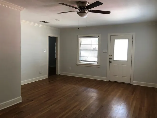an empty room with wooden floor fan and windows