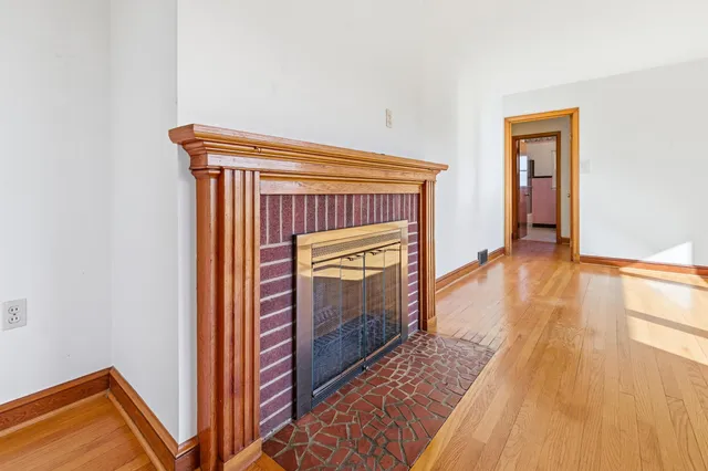 a view of an empty room with wooden floor a fireplace and a window