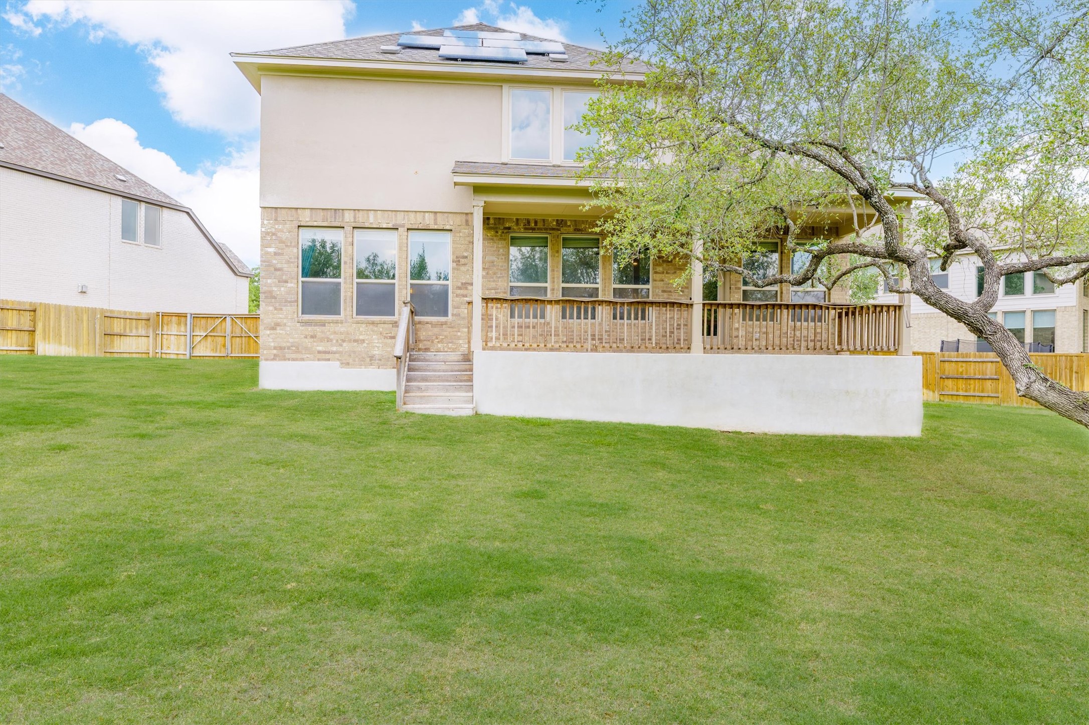 324 Autumn Oak Way Georgetown, TX 78628 - Photo 34 of 40 Expansive rear yard featuring a large green lawn, a multi-level exterior with brick and stucco finishes, a covered wood deck with railings, and established perimeter fencing