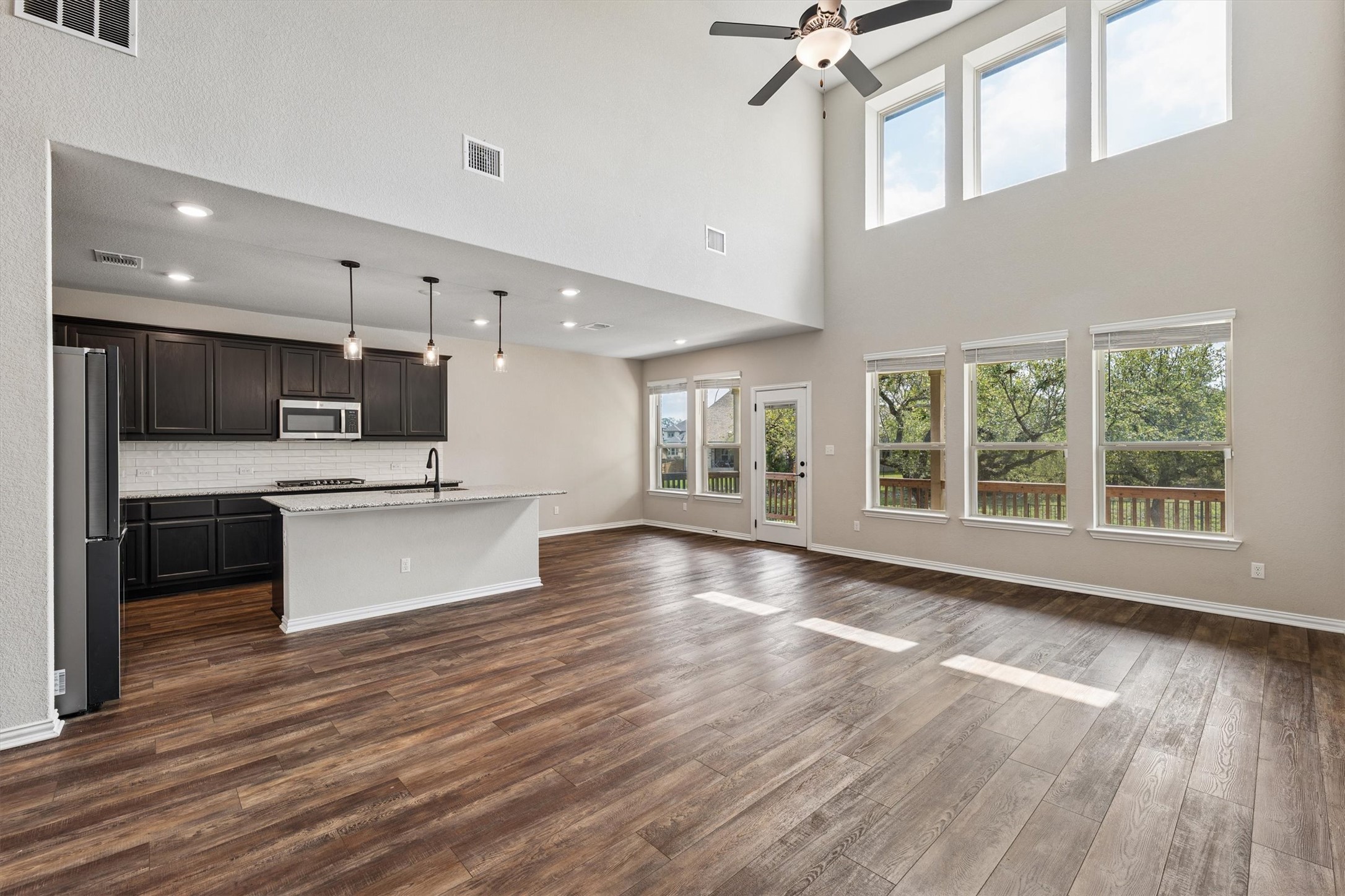 324 Autumn Oak Way Georgetown, TX 78628 - Photo 6 of 40 Open-concept living area featuring high ceilings, wood-finish flooring, a contemporary kitchen island with pendant lighting, dark cabinetry, and a full wall of windows