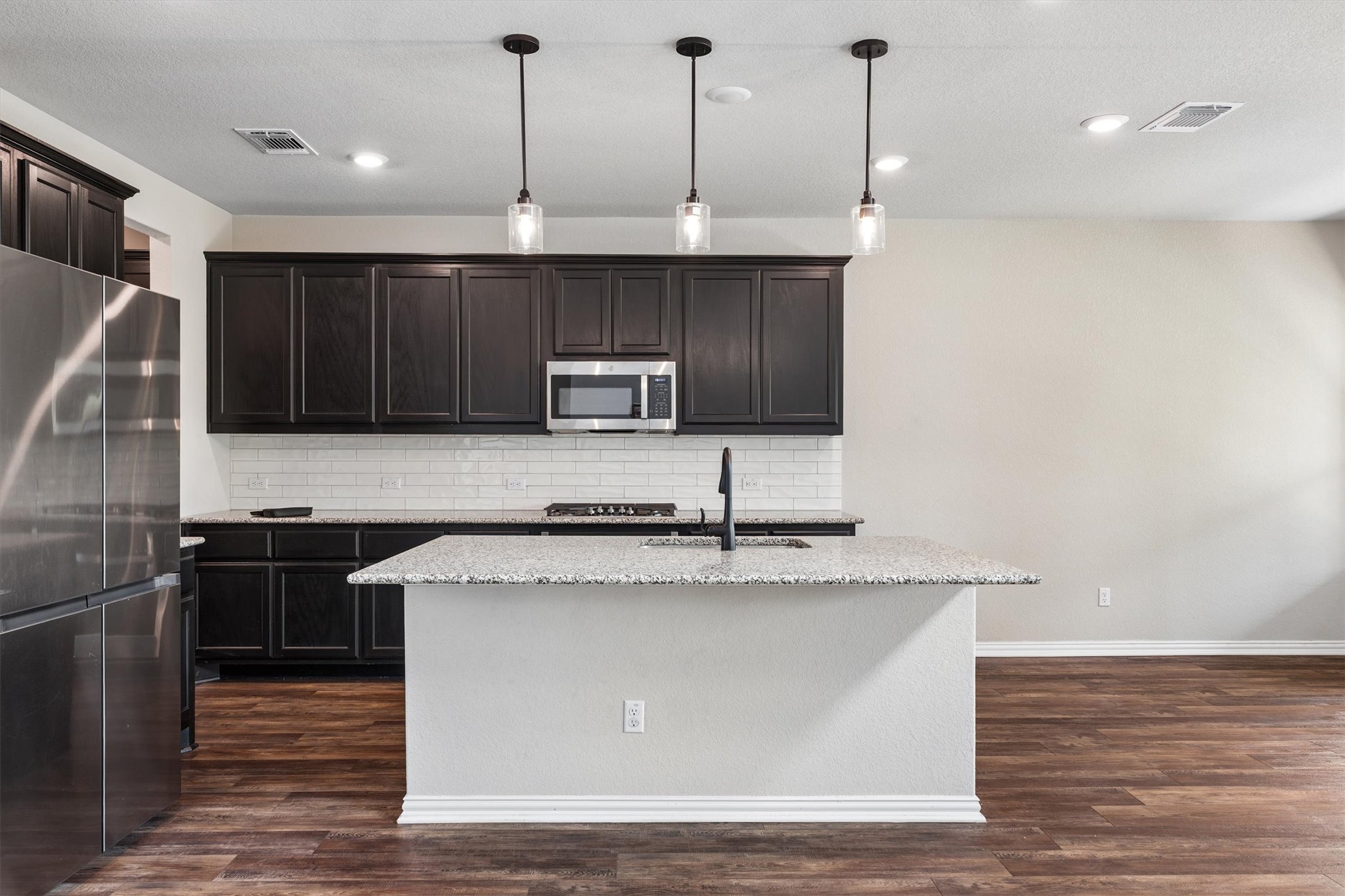 324 Autumn Oak Way Georgetown, TX 78628 - Photo 9 of 40 Kitchen featuring a central island with a sink, dark wood-finish cabinetry, stainless steel appliances, white subway tile backsplash, and overhead pendant lighting