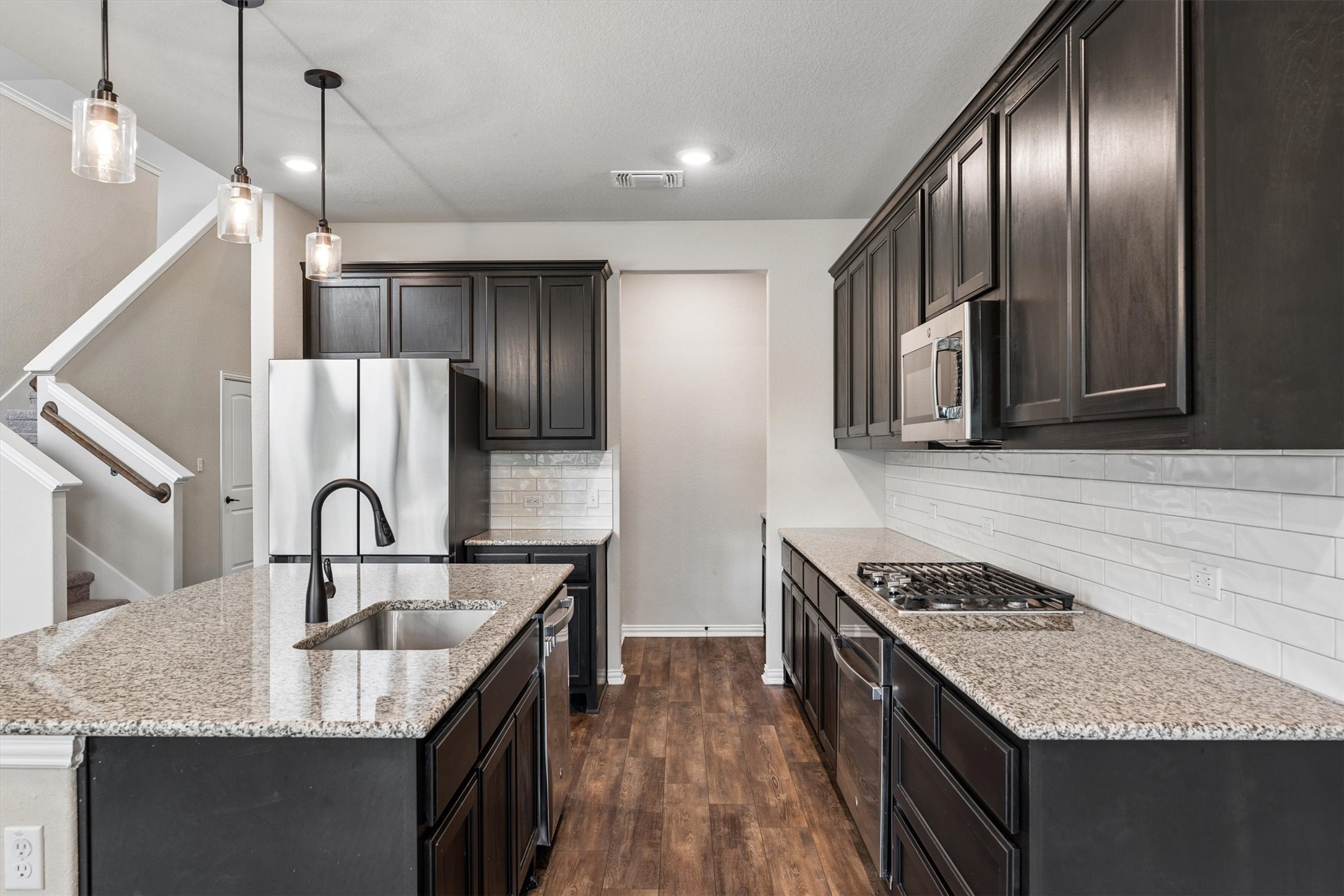 324 Autumn Oak Way Georgetown, TX 78628 - Photo 10 of 40 Kitchen featuring an island with a stainless steel sink and matte black faucet, granite countertops, dark wood cabinetry, stainless steel appliances, and wood-finish flooring