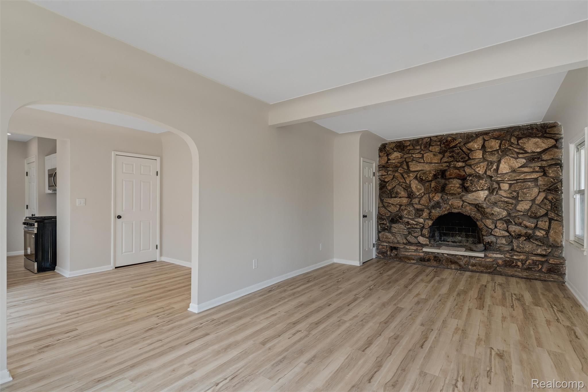 917 Perry Street Pontiac, MI 48340 - Photo 6 of 37 Unfurnished living room with arched walkways, a fireplace, light wood-style floors, and beam ceiling